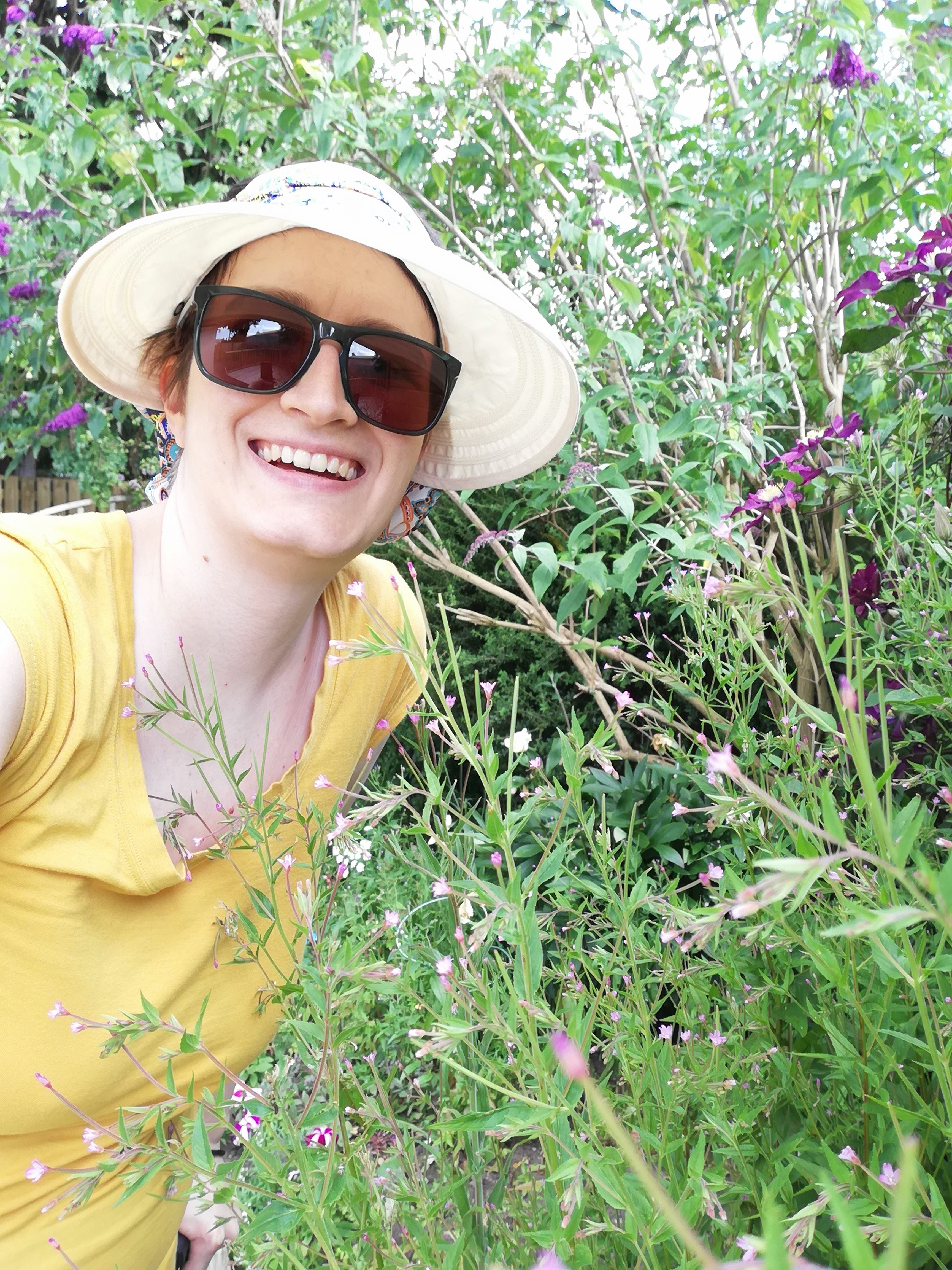 Char in the garden among the flowers. Wearing a sunhat and sunglasses.