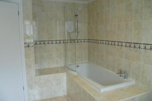 a large bathroom with a shower over the tub, walls and floors tiled with cream tiles.
