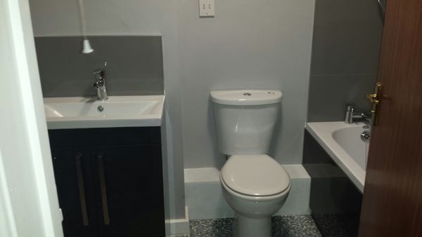 a small bathroom with basin on the left, toilet in hte middle and bath on the right, mosaic blue times on the floor