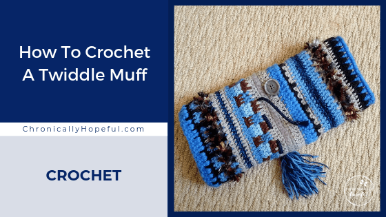 A crocheted twiddle muff with tassels and buttons on it lying on the carpet. Title reads, How to crochet s twiddle muff