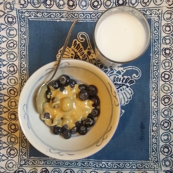 A bowl of blueberries and tahini and a glass of coconut milk to the right.