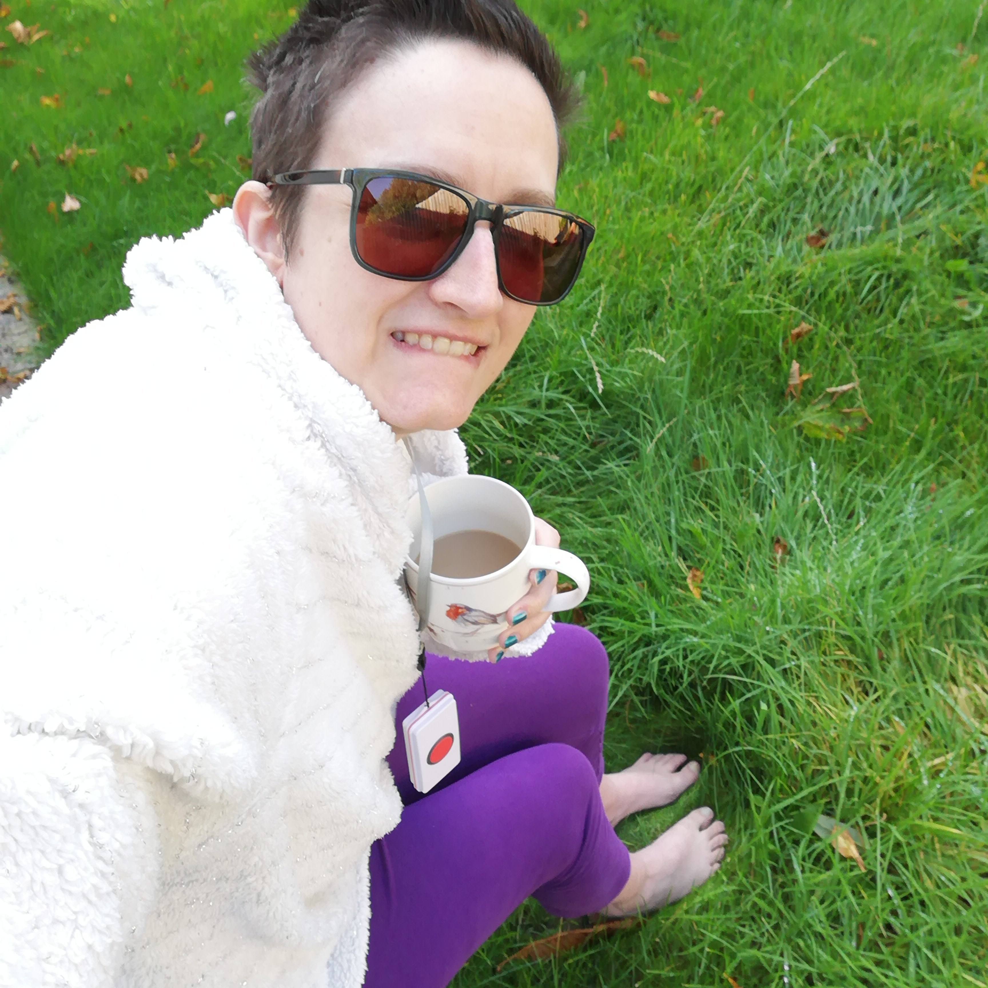 Char is sitting outside with a mug of coffee, her bare feet are on the grass.